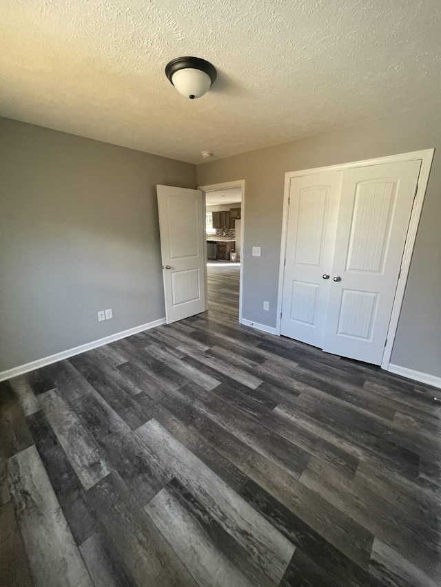 unfurnished bedroom with a textured ceiling, baseboards, and dark wood finished floors