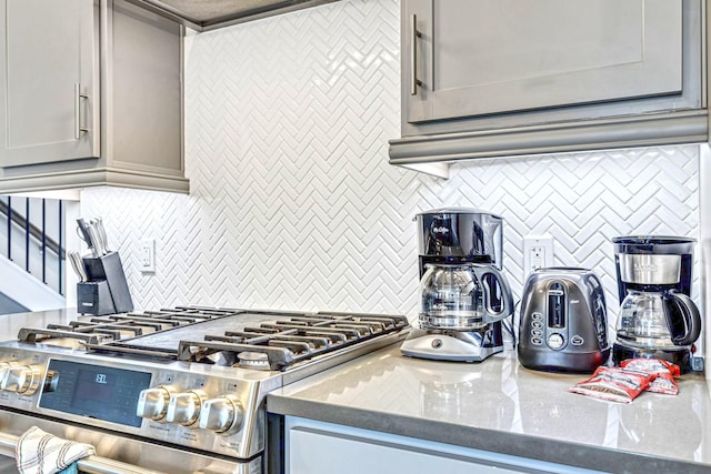 kitchen featuring gray cabinets, tasteful backsplash, stainless steel range with gas cooktop, and dark stone counters