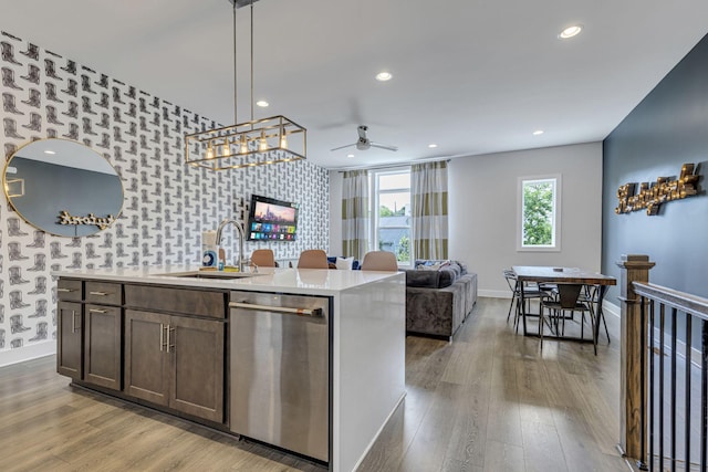 kitchen featuring pendant lighting, sink, stainless steel dishwasher, an island with sink, and wood-type flooring