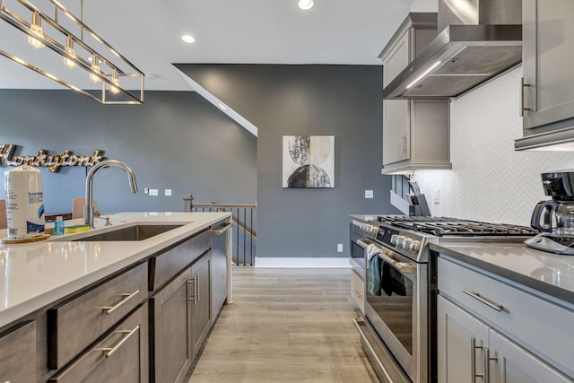 kitchen featuring stainless steel appliances, sink, wall chimney range hood, pendant lighting, and light hardwood / wood-style floors