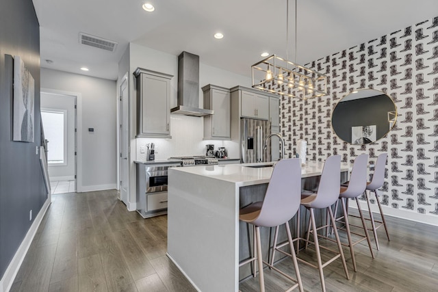 kitchen with a kitchen bar, gray cabinets, a kitchen island with sink, and wall chimney exhaust hood