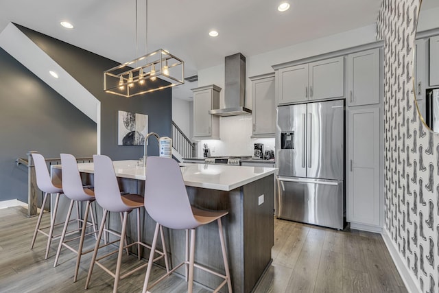 kitchen featuring wall chimney range hood, stainless steel fridge, pendant lighting, a kitchen bar, and gray cabinets