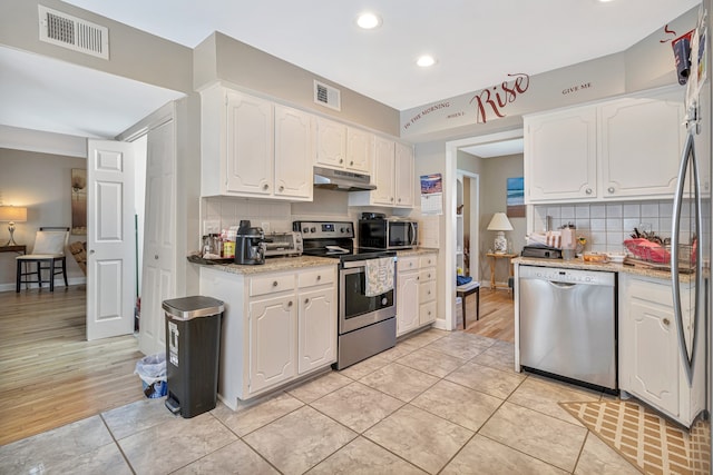 kitchen featuring light stone counters, light hardwood / wood-style flooring, tasteful backsplash, white cabinets, and appliances with stainless steel finishes