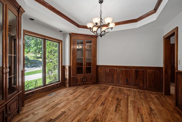 unfurnished dining area with hardwood / wood-style floors, a tray ceiling, ornamental molding, and a notable chandelier