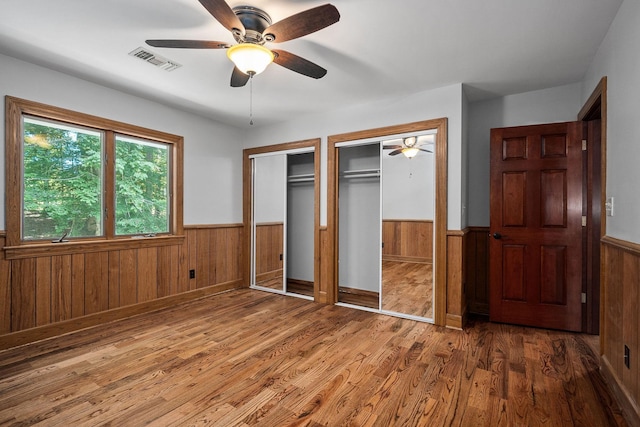 unfurnished bedroom featuring hardwood / wood-style flooring, ceiling fan, and multiple closets