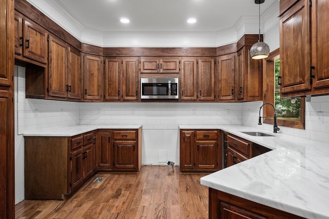 kitchen featuring light stone countertops, tasteful backsplash, sink, decorative light fixtures, and hardwood / wood-style floors