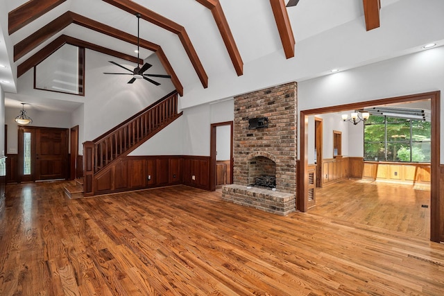 unfurnished living room with a fireplace, ceiling fan with notable chandelier, hardwood / wood-style flooring, high vaulted ceiling, and beamed ceiling