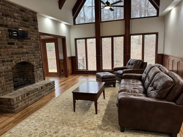 living room featuring high vaulted ceiling, a brick fireplace, ceiling fan, beam ceiling, and light hardwood / wood-style floors