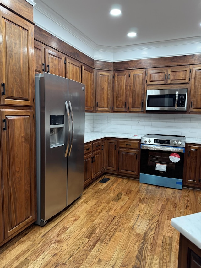 kitchen featuring ornamental molding, backsplash, stainless steel appliances, and light hardwood / wood-style floors