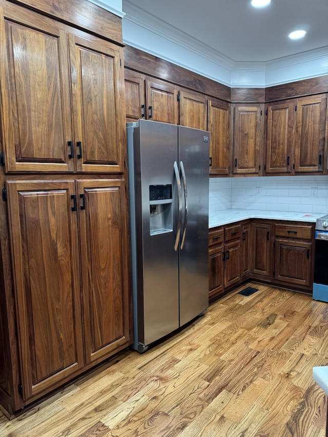 kitchen featuring light hardwood / wood-style flooring, stainless steel fridge, crown molding, decorative backsplash, and dark brown cabinets