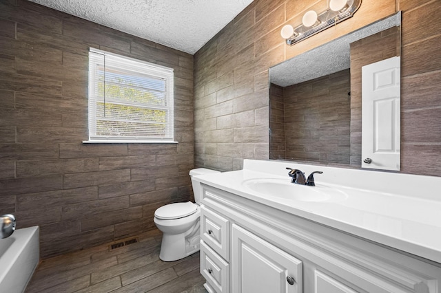 bathroom with a tub to relax in, vanity, a textured ceiling, tile walls, and toilet