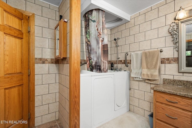 bathroom featuring tile walls, walk in shower, washer / dryer, and vanity