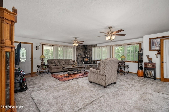 carpeted living room featuring a wood stove, plenty of natural light, ceiling fan, and a textured ceiling