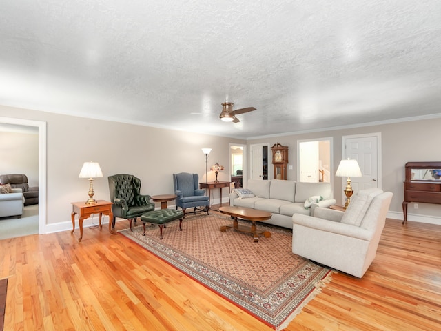 living room with light hardwood / wood-style floors, a textured ceiling, ornamental molding, and ceiling fan