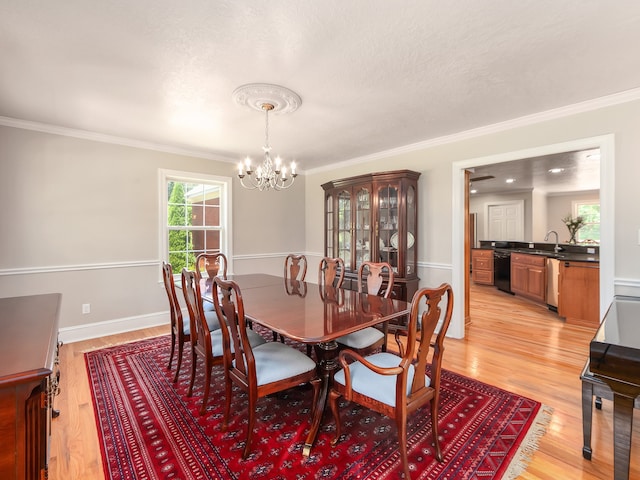 dining room with a notable chandelier, sink, light hardwood / wood-style flooring, and crown molding