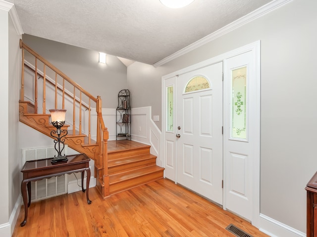 foyer entrance with light hardwood / wood-style flooring, a textured ceiling, and crown molding