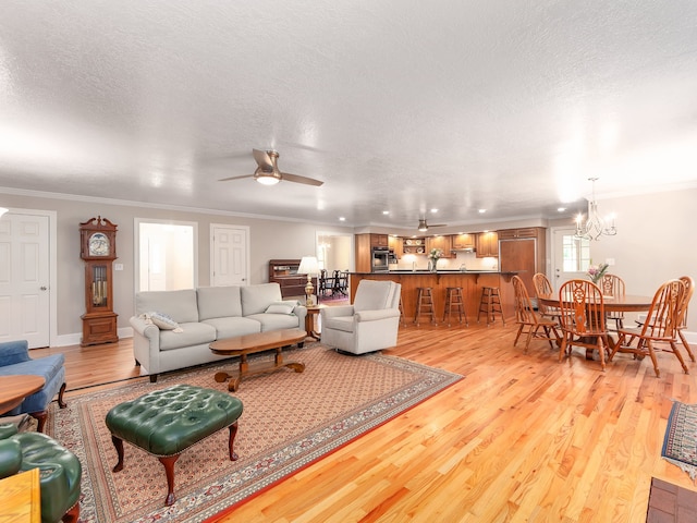 living room featuring ornamental molding, a textured ceiling, light wood-type flooring, and ceiling fan with notable chandelier