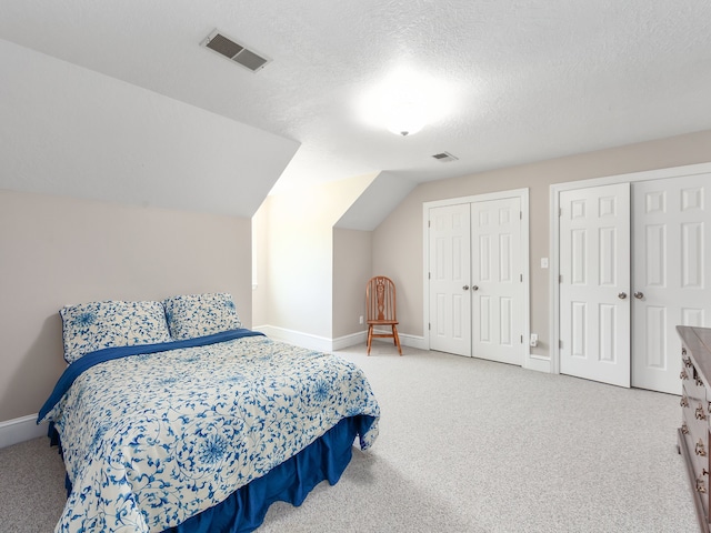 carpeted bedroom featuring two closets, a textured ceiling, and lofted ceiling