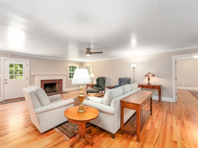 living room with light hardwood / wood-style floors, crown molding, a brick fireplace, and ceiling fan