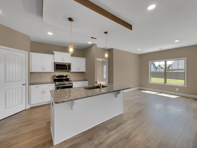 kitchen with white cabinetry, sink, stainless steel appliances, dark stone countertops, and a kitchen bar