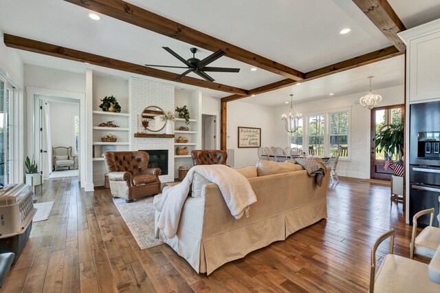 living room with ceiling fan with notable chandelier, built in features, a fireplace, beam ceiling, and dark hardwood / wood-style flooring