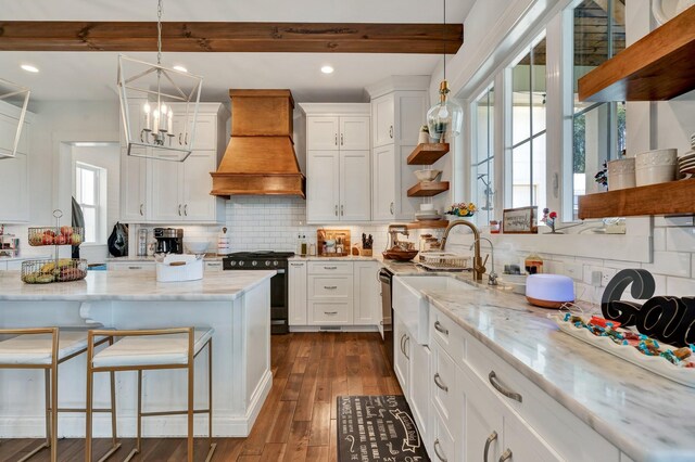 kitchen featuring light stone counters, custom exhaust hood, decorative light fixtures, stainless steel range oven, and white cabinetry