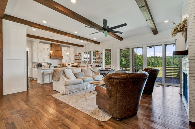 living room featuring beam ceiling, a brick fireplace, ceiling fan, and dark wood-type flooring