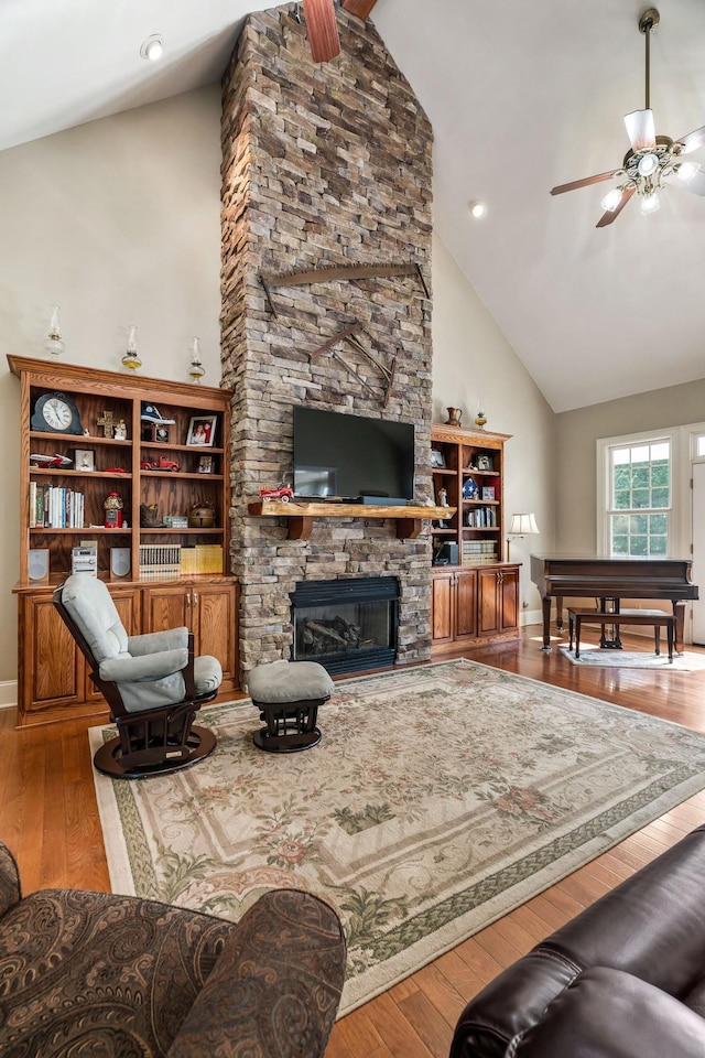 living room featuring hardwood / wood-style floors, high vaulted ceiling, a stone fireplace, and ceiling fan