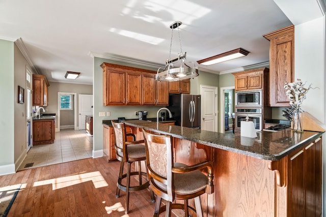 kitchen with pendant lighting, a breakfast bar, ornamental molding, kitchen peninsula, and stainless steel appliances