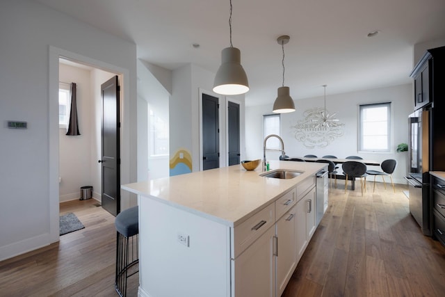 kitchen featuring sink, white cabinets, hanging light fixtures, hardwood / wood-style flooring, and a center island with sink