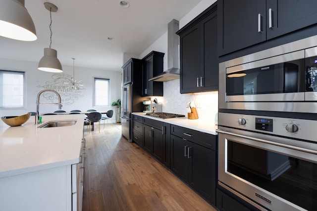 kitchen featuring sink, hanging light fixtures, appliances with stainless steel finishes, wall chimney range hood, and backsplash