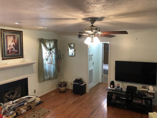 living area with a fireplace, a textured ceiling, and wood finished floors