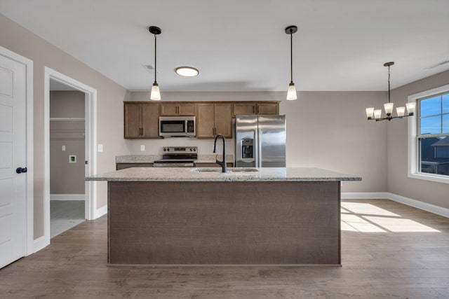 kitchen featuring wood finished floors, a sink, baseboards, appliances with stainless steel finishes, and pendant lighting