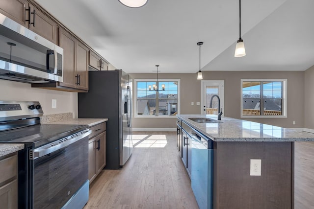 kitchen with a notable chandelier, stainless steel appliances, a sink, light wood finished floors, and decorative light fixtures