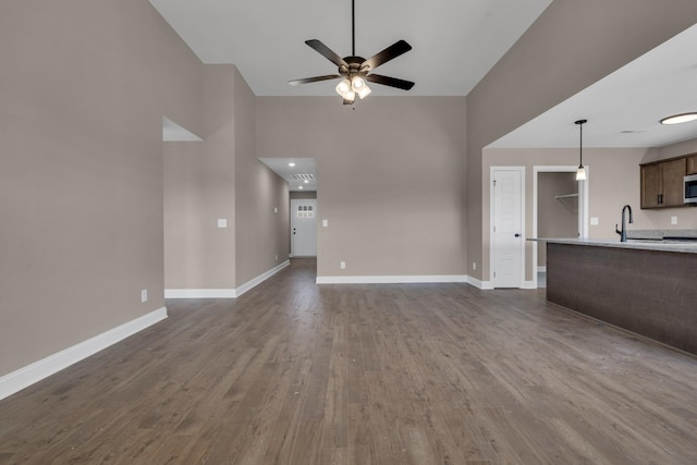 unfurnished living room featuring dark wood-type flooring, a sink, ceiling fan, and baseboards