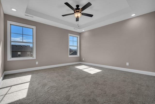 carpeted empty room featuring a raised ceiling, visible vents, and baseboards