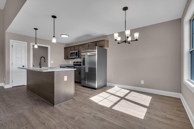 kitchen with wood finished floors, appliances with stainless steel finishes, a sink, and baseboards