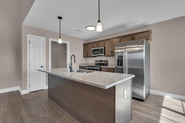 kitchen with appliances with stainless steel finishes, a sink, an island with sink, and wood finished floors