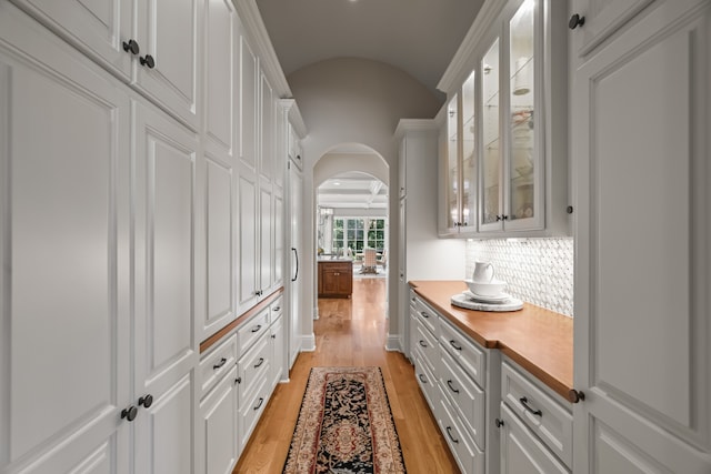 kitchen with white cabinetry, light hardwood / wood-style floors, lofted ceiling, wood counters, and backsplash