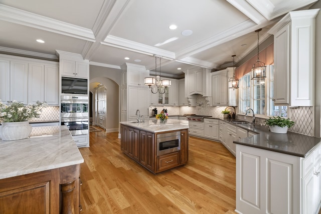 kitchen featuring an island with sink, decorative light fixtures, light wood-type flooring, backsplash, and appliances with stainless steel finishes