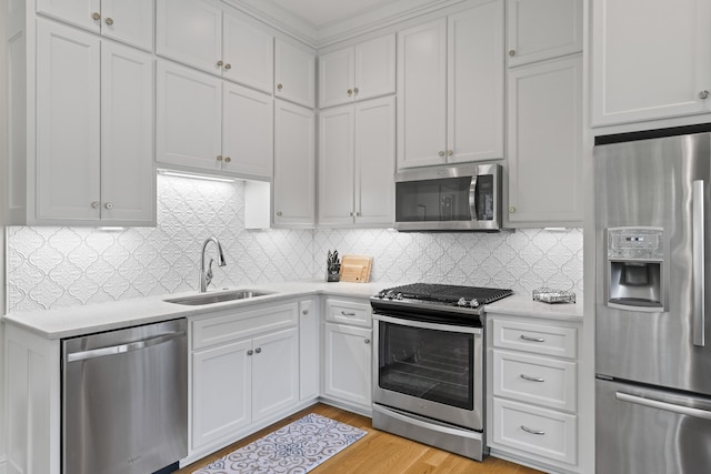 kitchen with white cabinets, stainless steel appliances, tasteful backsplash, light wood-type flooring, and sink