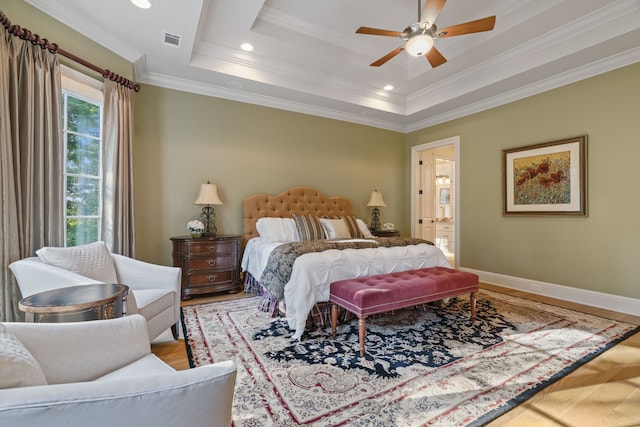 bedroom with crown molding, hardwood / wood-style flooring, ensuite bathroom, ceiling fan, and a raised ceiling