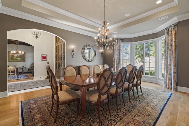 dining area with a notable chandelier, a tray ceiling, crown molding, and light hardwood / wood-style flooring