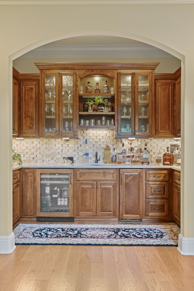 bar with backsplash, light wood-type flooring, sink, and beverage cooler