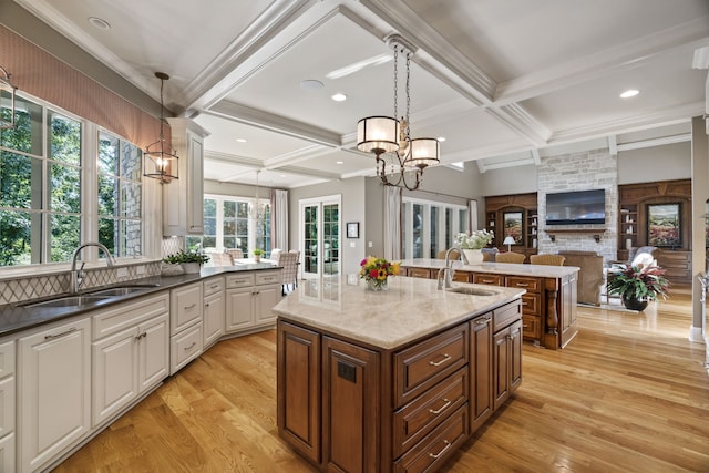 kitchen with a center island with sink, decorative light fixtures, sink, and light wood-type flooring