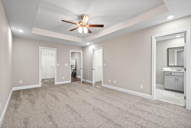 unfurnished bedroom featuring ensuite bathroom, ceiling fan, a raised ceiling, and light carpet