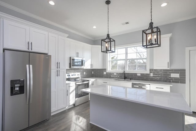 kitchen with a center island, sink, hanging light fixtures, appliances with stainless steel finishes, and white cabinetry