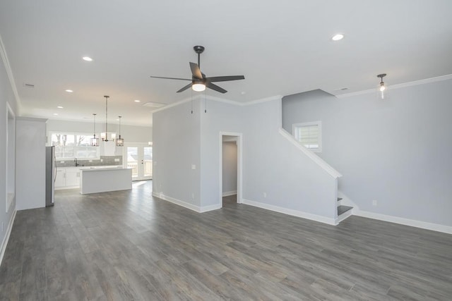 unfurnished living room with sink, dark wood-type flooring, ceiling fan with notable chandelier, and ornamental molding