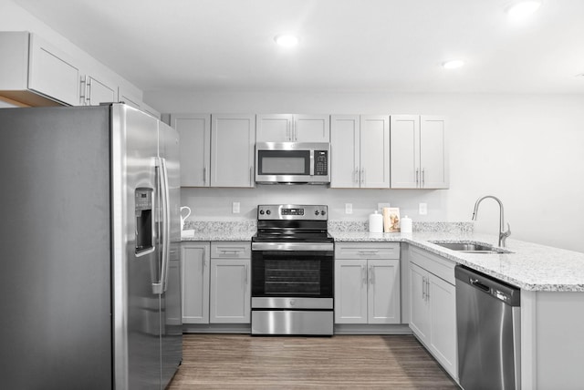 kitchen with appliances with stainless steel finishes, light stone counters, wood finished floors, a peninsula, and a sink