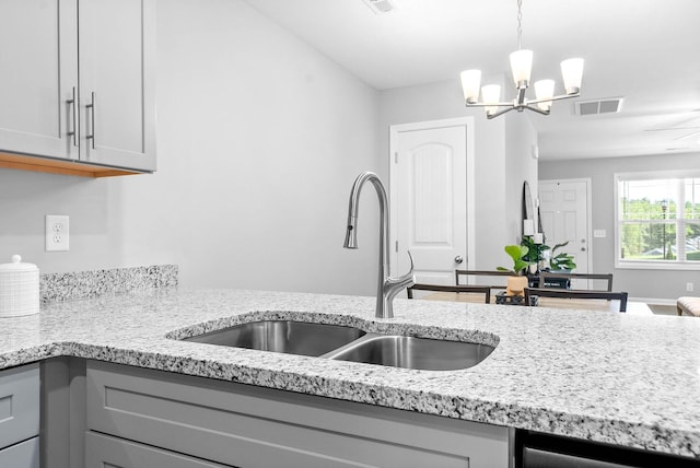 kitchen with light stone counters, gray cabinets, visible vents, an inviting chandelier, and a sink